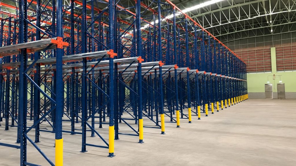 Industrial drive-in pallet racking system with deep storage lanes and protective column guards in a warehouse.